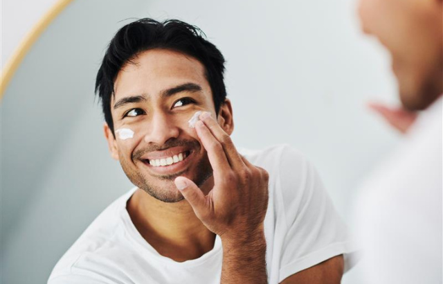 man smiling into mirror while applying moisturizer to his face