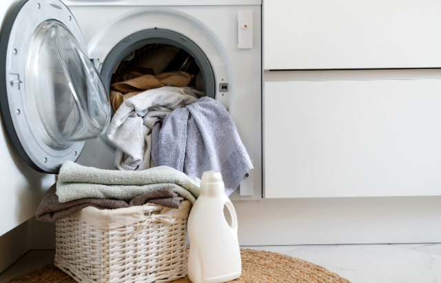 washing machine filled with laundry and basket with soap in front of it