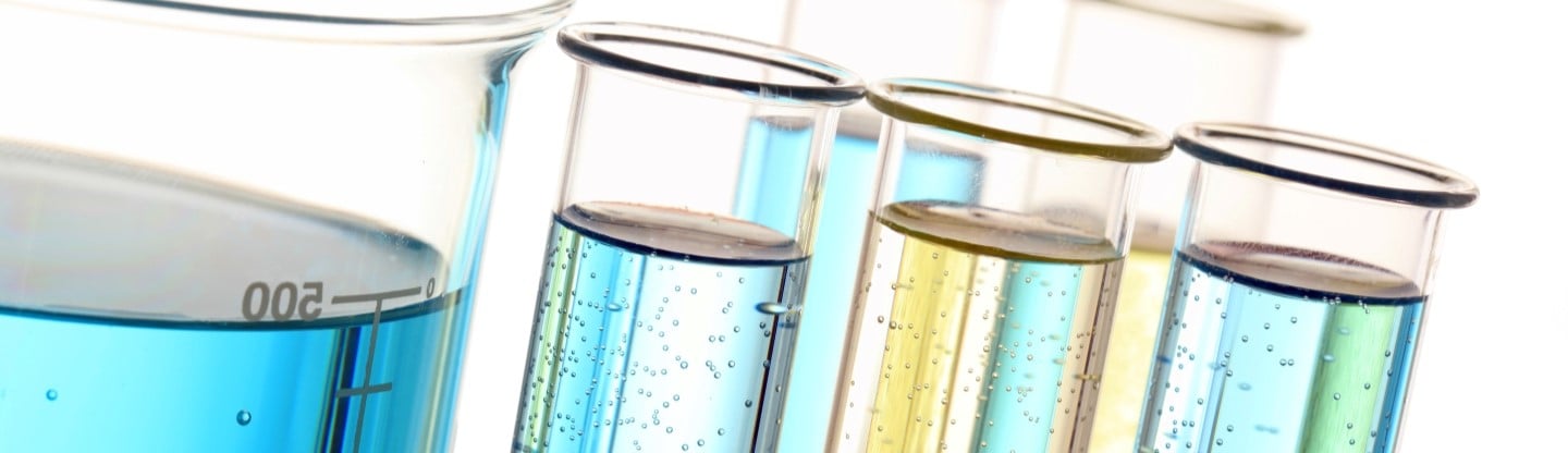 Beakers filled with lightly colored fluid in front of a bright white background