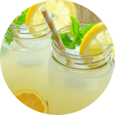 Two single serve jars filled with iced lemonade, lemon wedges, basil, and a paper straw