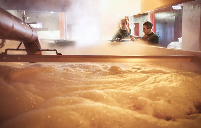 Brewers working over foamy beer brewnig in large vats