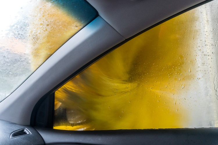 The view from inside of a car looking out of the passenger window as a large yellow brush dries passenger side of the vehicle.