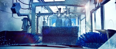 The view from the drivers seat of an automobile going through a tunnel car wash with large brushes cleaning the hood and sides of the vehicle.