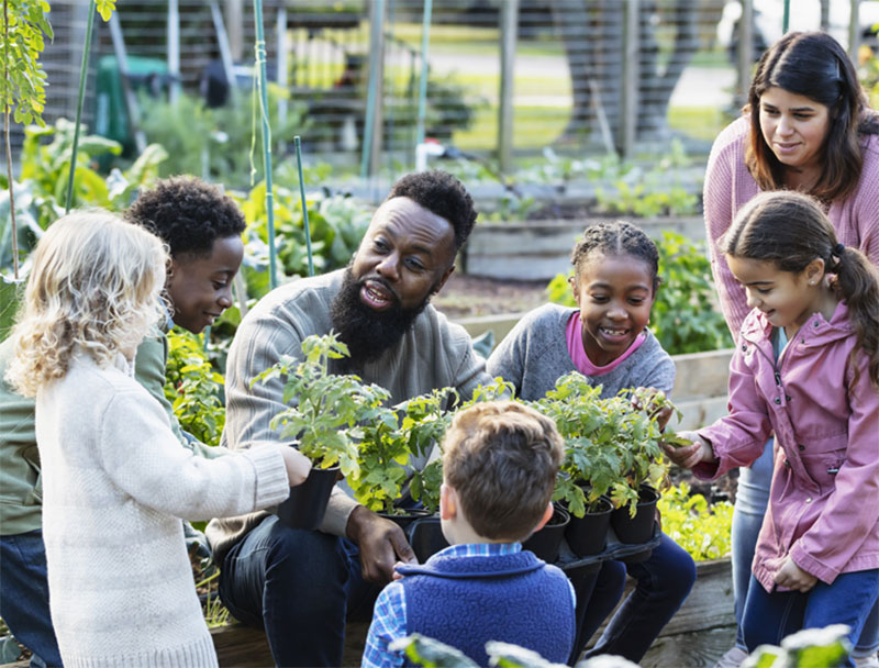 A man teaches a group of children about sustainability at a community garden