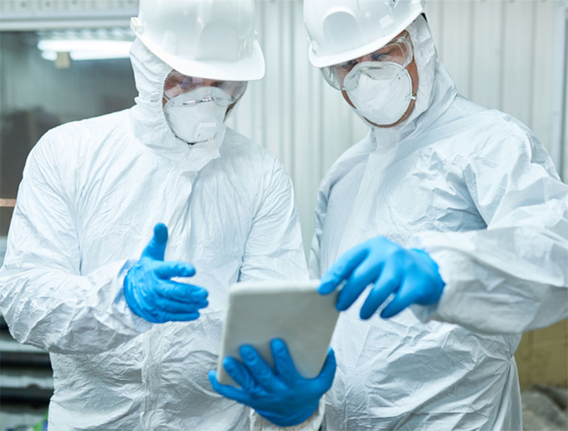 Two men in a warehouse wearing full PPE, review a list of safer substitute products for distribution