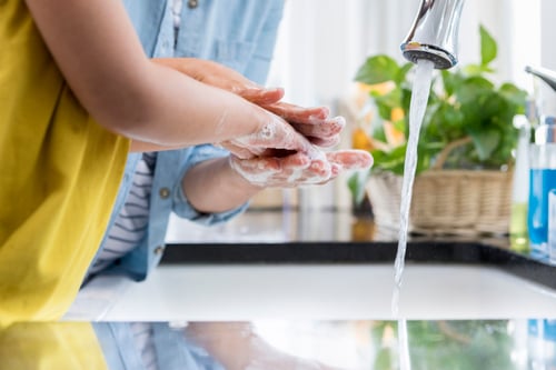 adult helping a child in a yellow shirt wash their hands in the kitchen sink