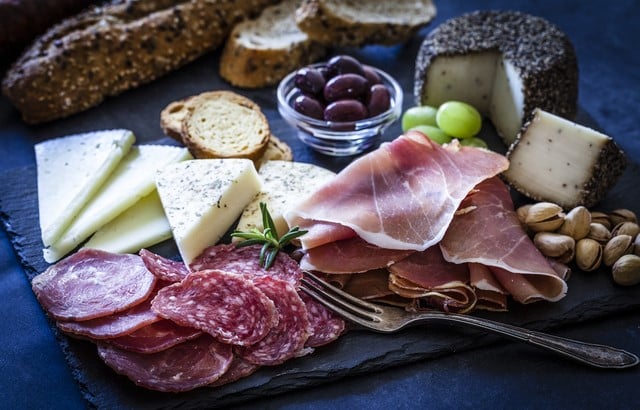 various meats, cheeses, olives and bread on a slate charcueterie board