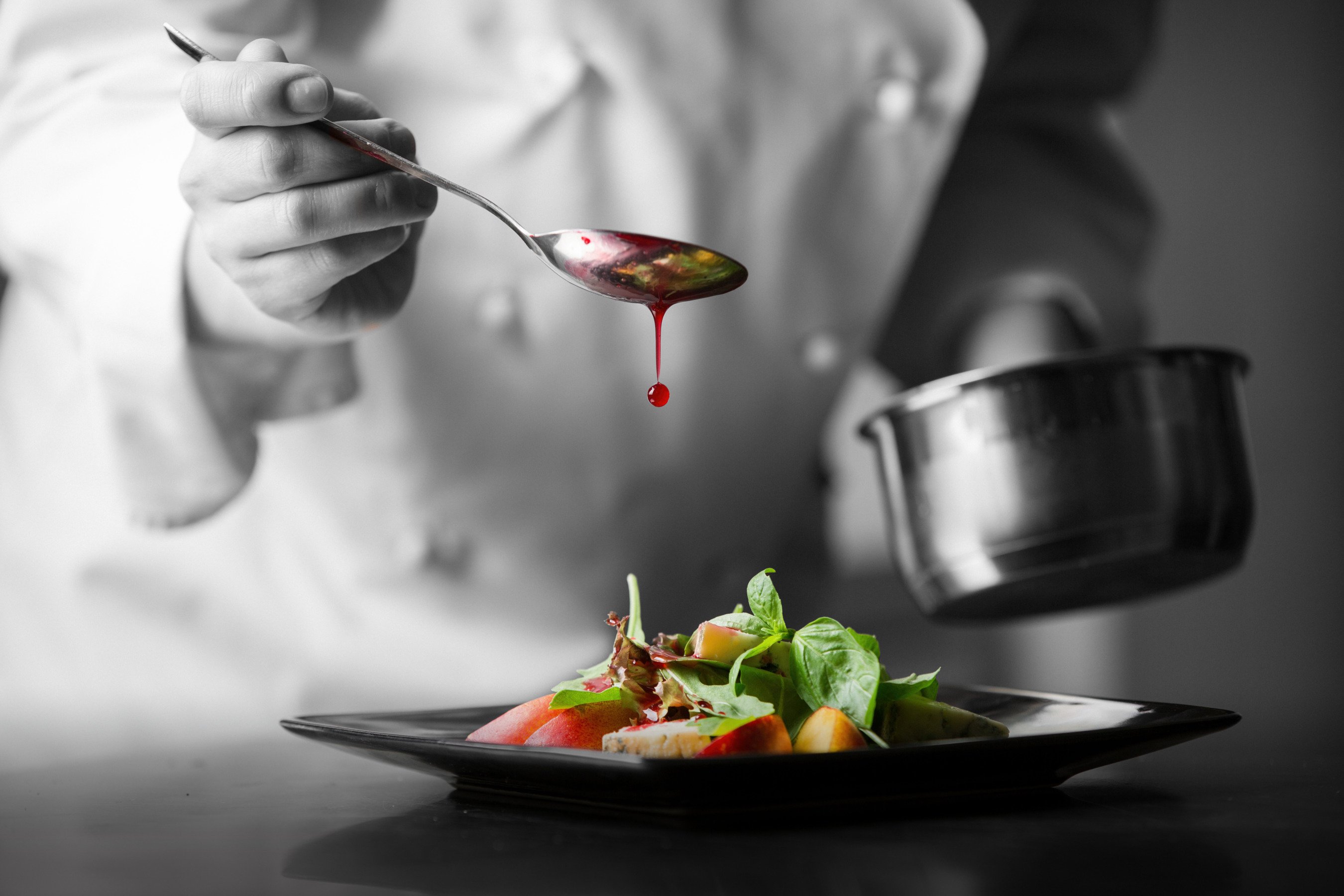 Close up of a chef's had as he drizzles sauce from a spoon over a salad dish created at The Hatchery Chicago