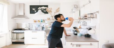 man drinking in his kitchen after a workout