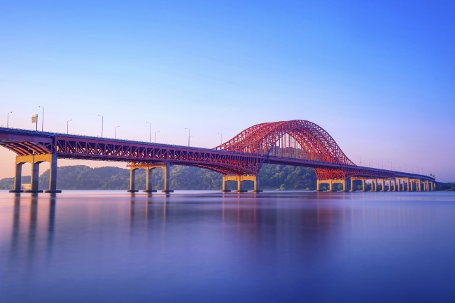 A bridge painted red with sustainable coatings spans a calm lake