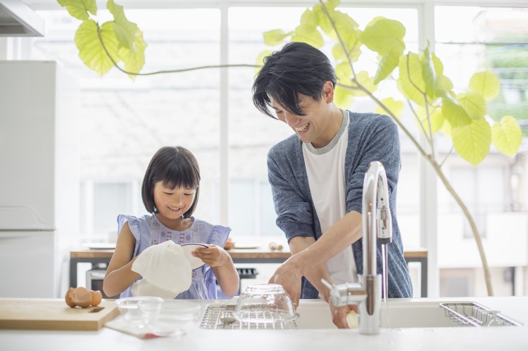 A father and daughter standing at the kitchen sink in a clean bright kitchen washing dishes together