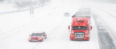 car and distribution  truck driving on a snow covered roadway