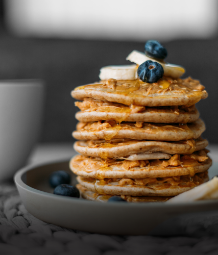 A stack of healthier ingredient pancakes on a plate with bananas and blueberries