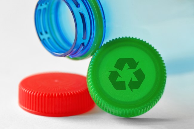 A plastic recyclable bottle lays next to a plastic green cap with the recycle, reduce, reuse arrows printed on top