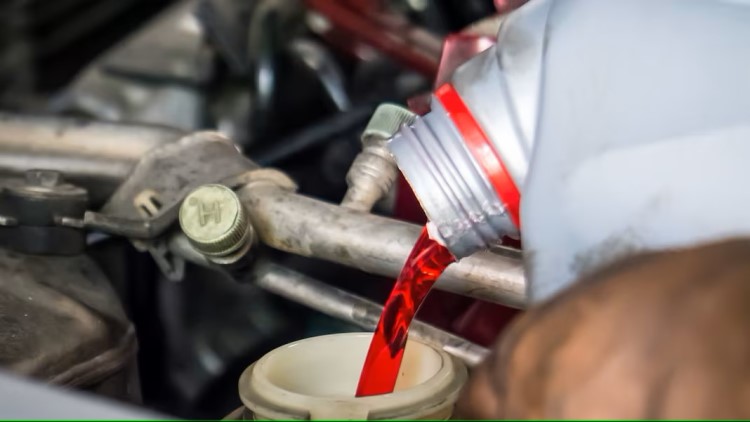 A container of red transmission fluid pouring into the transmission of a vehicle