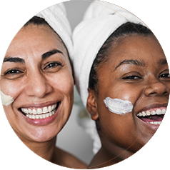 Two women with skin care products on their cheeks smile