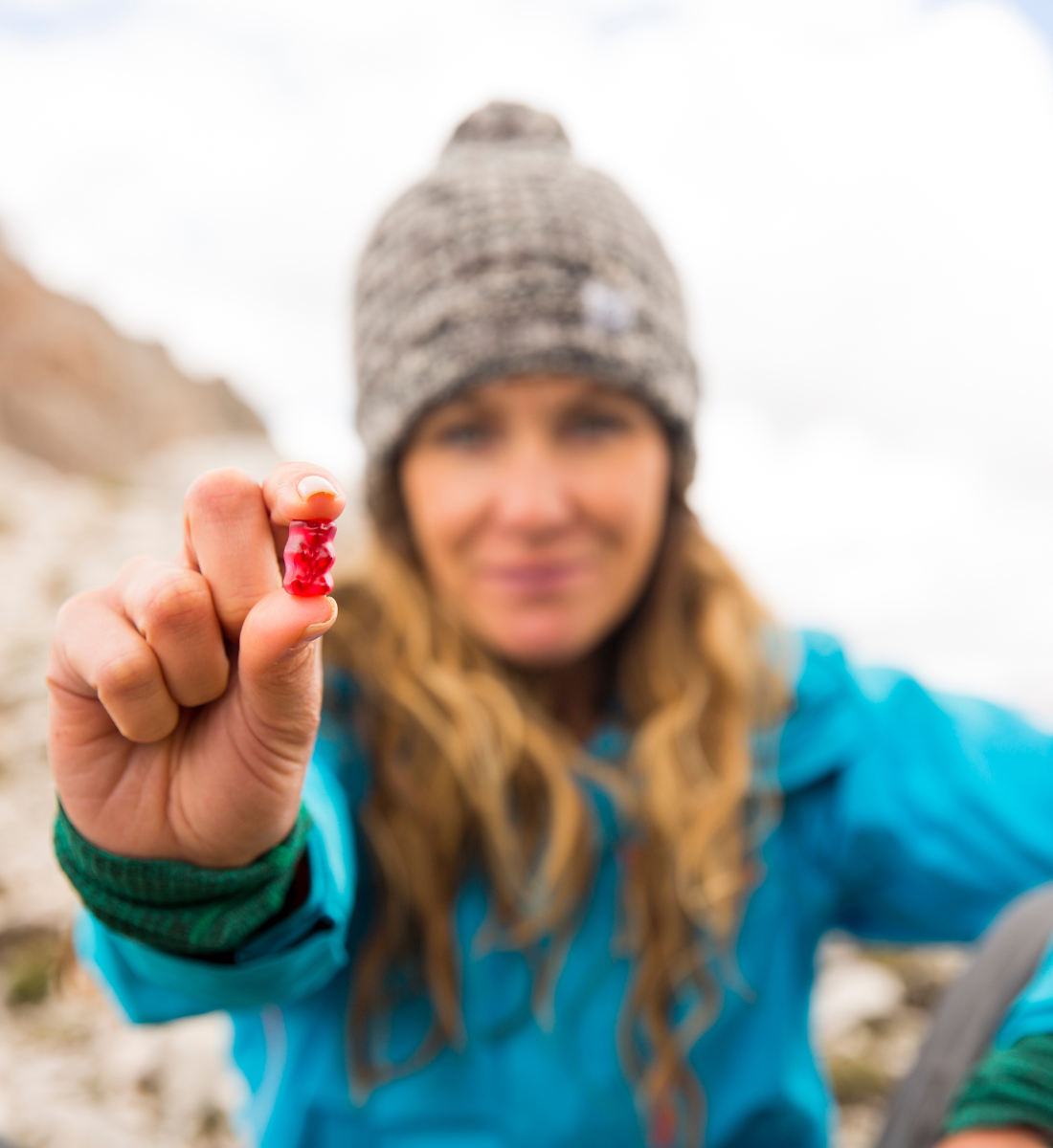 A woman in winterwear and a snow cap holds up a sports nutrition supplement to boost her athletic performance while hiking in the mountains.