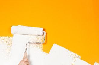 A yellow wall in the process of being painted white with a paint roller