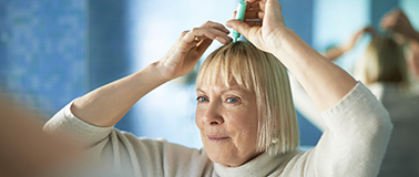 A woman applying a topical treatment to her scalp.