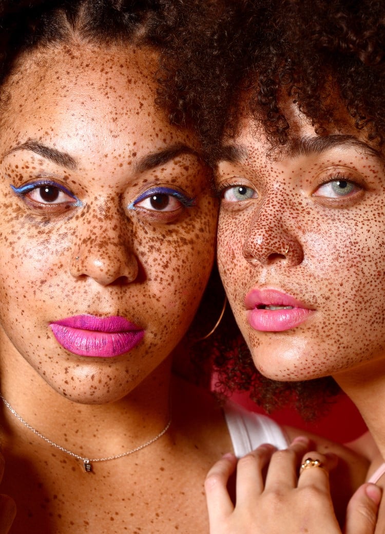 Two freckled women staring forward wearing bold eye and lip makeup