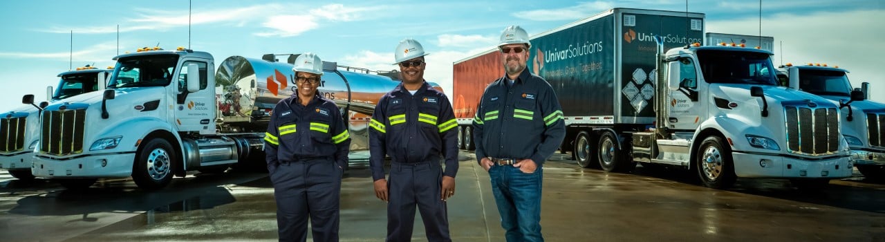 Three Univar Solutions employees standing in front of a fleet of transportation vehicles