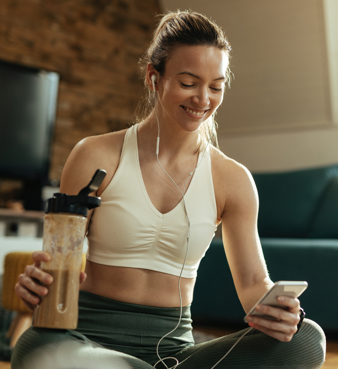  A young woman in workout clothes enjoys a smoothie just before doing a workout in her living room.