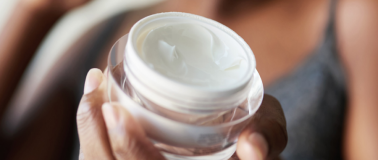 A blurred person holds a jar of moisturizer in clear view