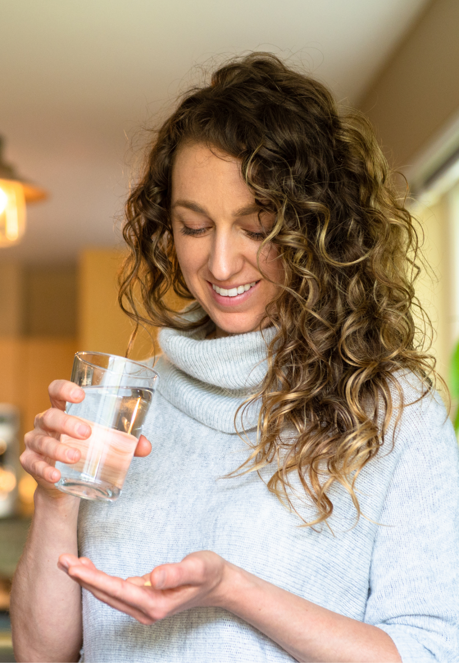 Young smiling woman in her fashionable living room about to take a prescription medication while holding a tablet in one hand and a glass of water in the other.
